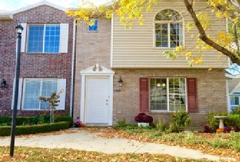 This two-story townhouse at 2874 W 1170 N Provo features a brick and siding exterior, large windows, a white front door, and a landscaped garden with autumn leaves. A lamppost and tree complete the picturesque setting.