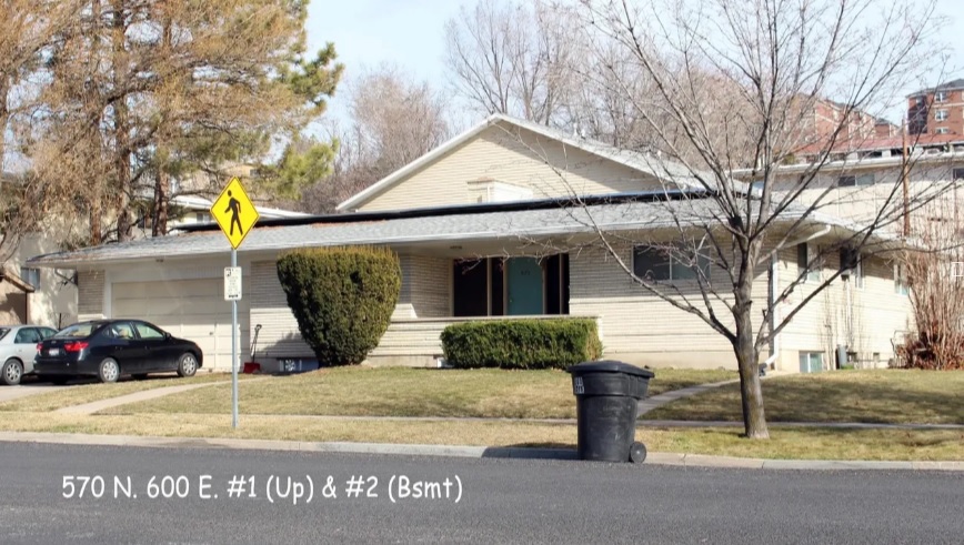 Single-story beige house with a gray roof, front porch, and trimmed bushes on a corner lot in Autumn Hills. Several parked cars, a trash bin on the curb, and bare trees. Text over the image displays 560 Logan.