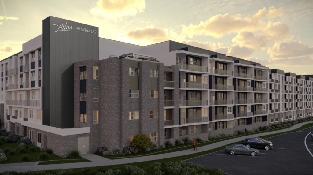 Modern mid-rise apartment building with balconies, named Atlas Alvarado, at sunset. Two parked cars and a person walking on the sidewalk are visible in front of the building, with landscaped greenery around.