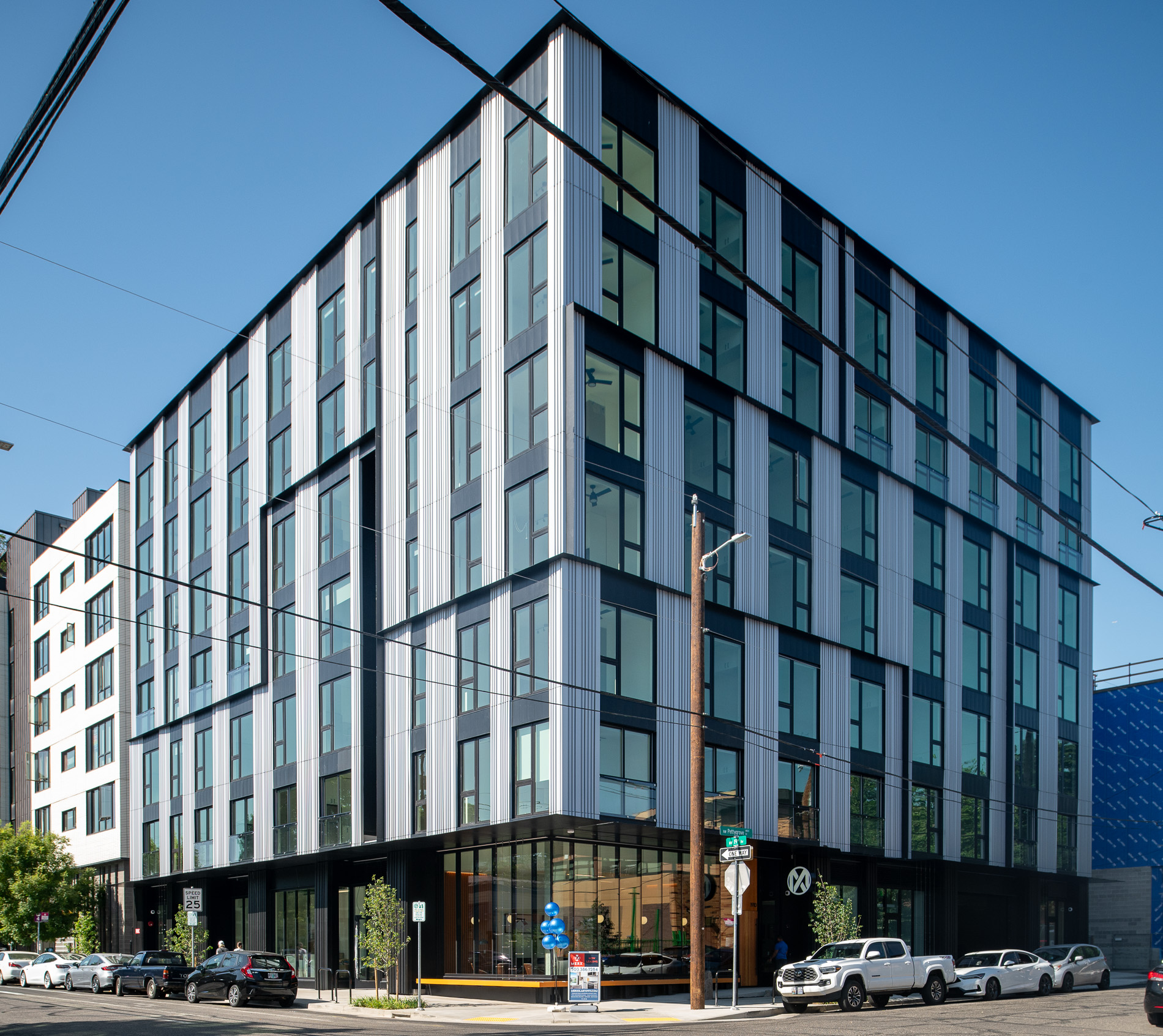 MERX Slabtown is a modern six-story building with large windows and a striped gray facade, standing on a city corner. Cars are parked along the street, and power lines cross overhead under a clear blue sky.